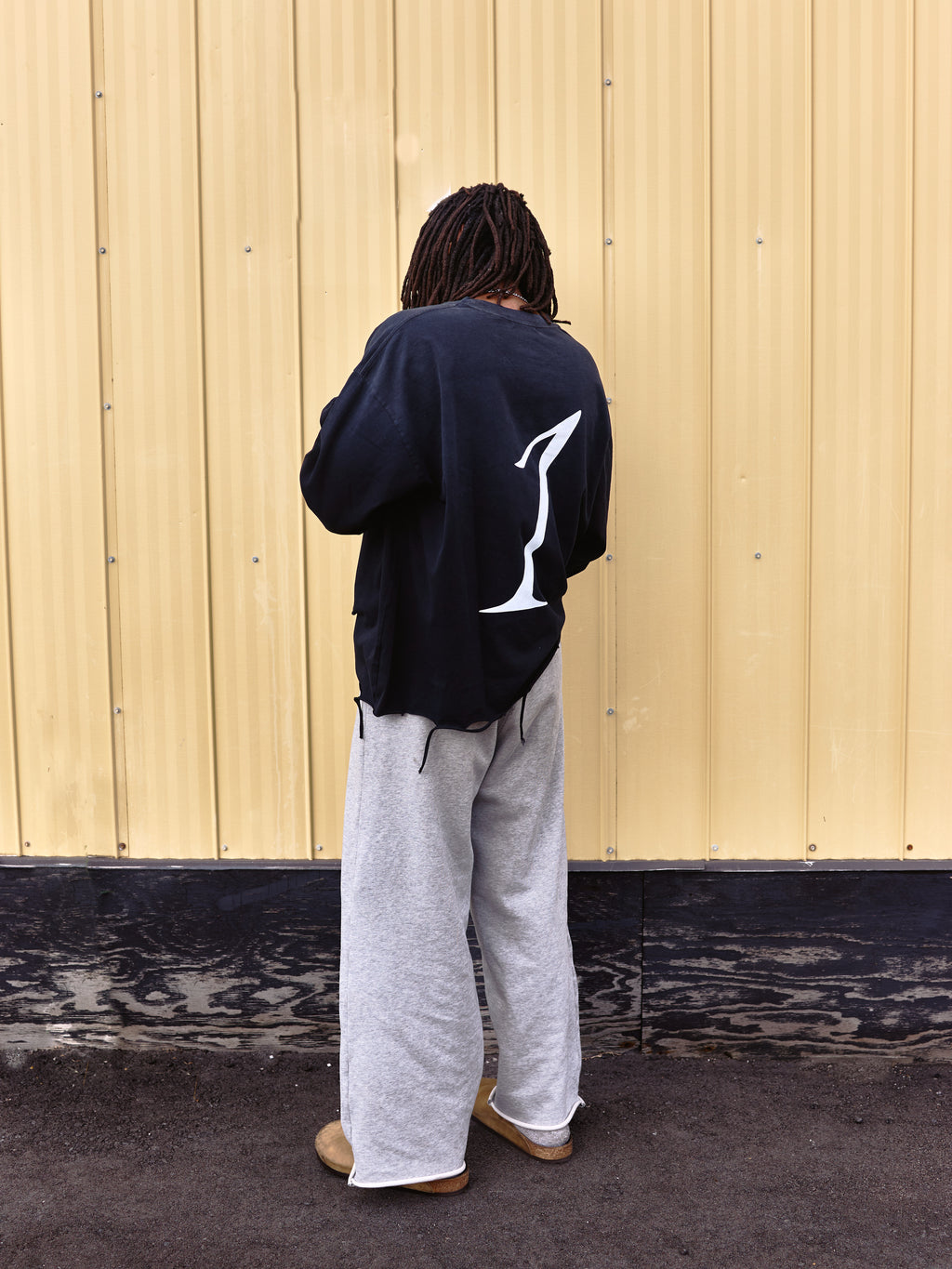 Person wearing a black sweatshirt with a white logo on the back, standing against a beige wall.