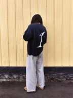 Person wearing a black sweatshirt with a white logo on the back, standing against a beige wall.